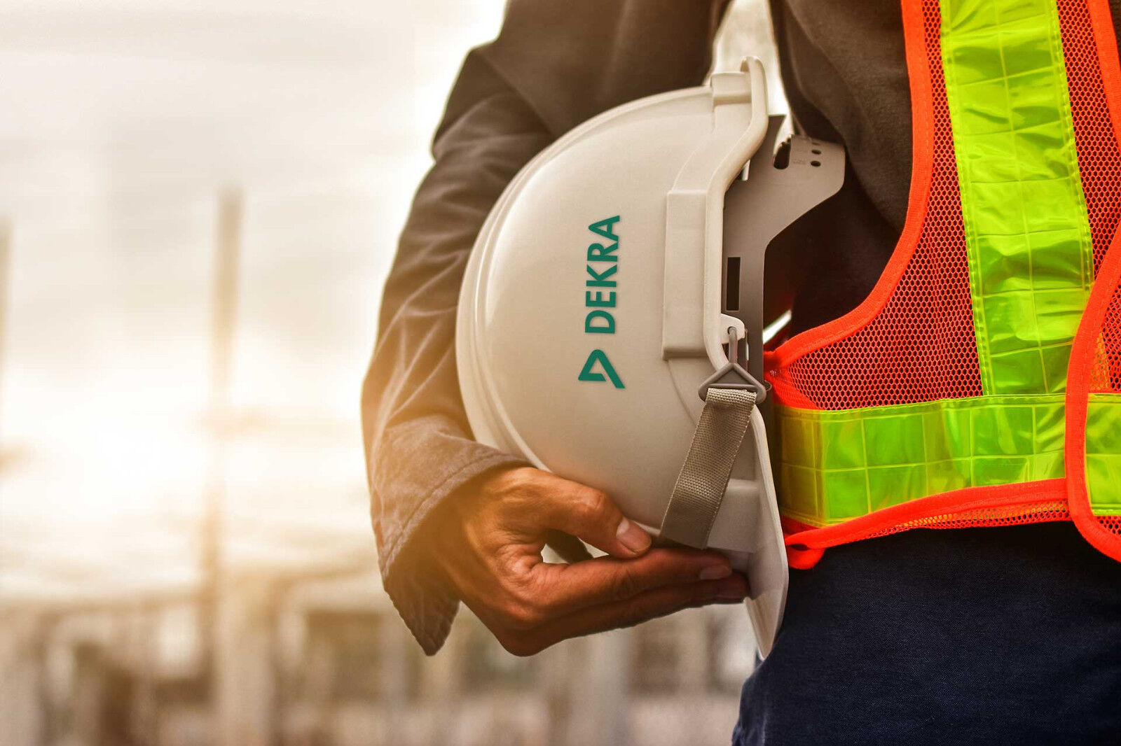 One arm holds a white safety helmet bearing the inscription DEKRA.