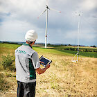 A DEKRA engineer with a tablet in his hand. Two wind turbines can be seen in the background.